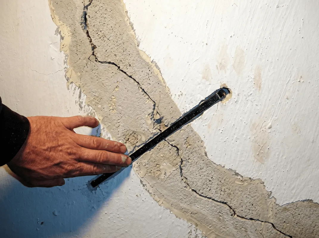 A wall with a large crack is being inspected by a professional in Little Rock, AR